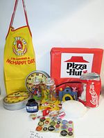 Group shot showing entire lot with apron, Pizza Hut bag, jars, tins, toy camera, Coke plush and pins