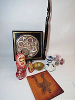 Group shot showing all items including matryoshka dolls, brass bowl, leather cover, porcelain flower, mosaic plaque and glass pieces