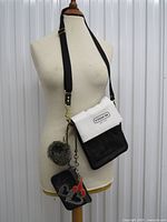 Full view of crossbody bag on mannequin showing strap, wristlet, pom, charms