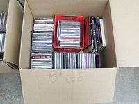 Cardboard box containing stacks of CDs in jewel cases and red tray