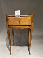 Front view of wooden side table showing drawer, scalloped back edge and tapered legs