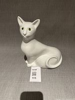 Front view of glossy white ceramic cat figurine with green eyes, tail curled
