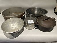Group view of aluminum pan, two colanders, two camping pots, cast iron Dutch oven with lid