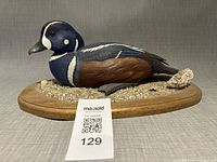 Left profile of carved harlequin duck on oval base with lot tag visible