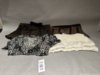 Four garments laid flat: lace dress, knit dress, brown skirt, white pleated skirt with lot tag 104