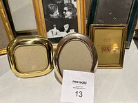 Group of small metal frames, includes brass square, silver oval, and gold rectangular plus others in background
