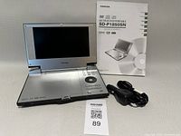 Open Toshiba SD-P1850SN player with screen visible, manual booklet and car charger alongside