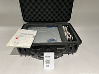 Projector inside protective case with manual, cords visible