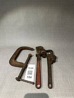 Overview of C-clamp and two pipe wrenches on tabletop