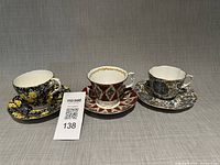 Three cup-and-saucer sets displayed side by side showing patterns and overall condition