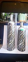 Two tall cylindrical vases with zebra stripe pattern shown side by side against ruler