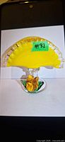 Front view showing yellow fan panel, clear ruffled edge, green stem, yellow flower and base