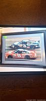 Framed color photo print showing both Earnhardt cars; black frame, grey mat