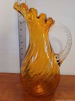 Full view of amber swirl glass pitcher beside ruler
