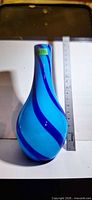 Front view of light blue glass vase with dark blue swirl, ruler beside for scale
