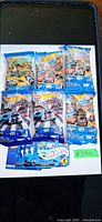 Six opened Hot Wheels Mystery Models foil packs with separate sticker sheet card on white background