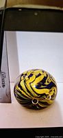 Overall view of round yellow and blue swirl glass paperweight showing controlled bubbles and exterior nick