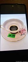 Teacup resting in saucer showing color, rose motif, black center, gold trim