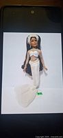 Full view of porcelain mermaid doll in white costume on plain background