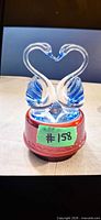 Front view of clear and blue glass swans on red music box base