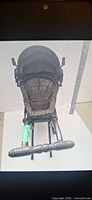 Front view of wicker baby carriage showing handle, seat and wheels