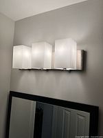 Fixture illuminated, showing three frosted glass shades on brushed nickel bar