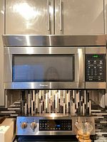 Front view of stainless steel Magic Chef over-the-range microwave installed above stove, control panel illuminated