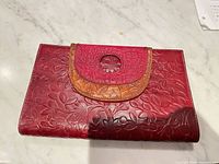 Front view of red floral-embossed leather clutch with brown-tan trimmed flap