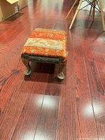 Three-quarter view of footstool showing carved legs, fabric top