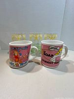 Two printed ceramic mugs in front of three tennis-themed glasses