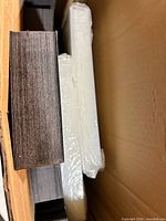 Cardboard shipping carton containing stacks of flat black box bases and separate clear plastic lids wrapped in film