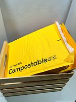 Wooden crate filled with yellow 100% compostable padded mailers showing peel-and-seal strips