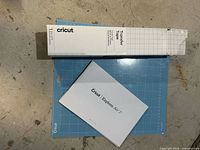 Blue cutting mat, white transfer tape box, white manual displayed on floor