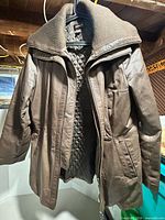Front view of brown Danier leather coat hanging, showing collar, zipper, pockets, and quilted lining