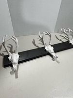 Full view of wall-mount coat rack showing three deer skull hook forms on black rail