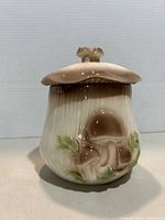 side view of mushroom-shaped ceramic jar with lid showing mushroom relief and green accents