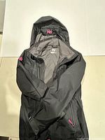 Full view of black Helly Hansen hooded coat showing front, lining, pockets, and HH logos