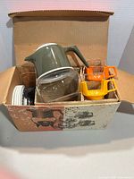 Open box showing carafe, cups in holders, warming stand parts