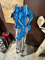 Folded blue canopy tent with metal legs secured by strap