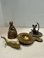 All four brass items grouped: lady bell, handled dish, whale figurine, cat on tray