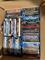 Open box showing rows of Blu-ray and DVD cases with visible titles