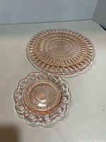Two pink pressed glass plates showing starburst pattern and scalloped/open-lace rims