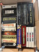 Box containing mixed VHS tapes and DVD cases with visible titles