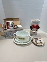 All items grouped: boxed mugs, gravy boat with plate, Minnie vase, stack of hockey dishes