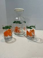 front view of pitcher with lid and two matching glasses showing orange graphics