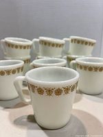 Front view showing multiple white mugs with gold floral band