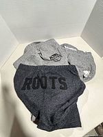 Three pairs of Roots sweatpants stacked showing logos and colours