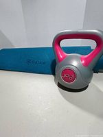 Blue Gaiam yoga mat and grey/pink Jogi 10 lb kettlebell on white surface