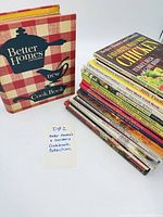 Group shot showing red gingham binder standing and stack of 18 hardcovers