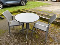 Full view of round metal table with two sling chairs on patio